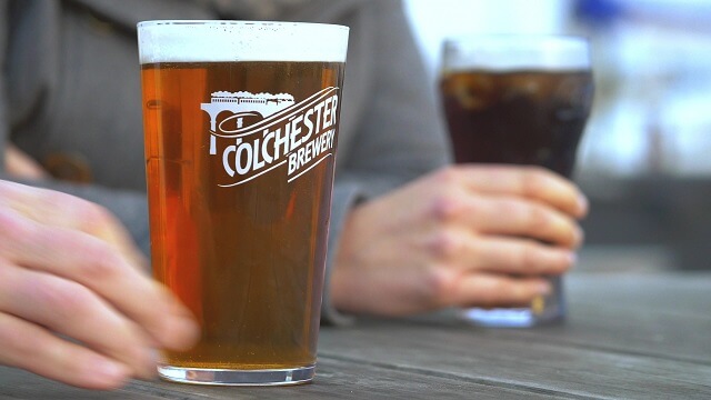 2 pints of beer rested on a table with Colchester Brewery branding on the glass